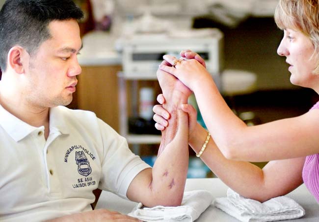 Ingrid Loney,  Hand Therapist - COTA (Certified Occupational Therapy  Assistant), works with Duy Ngo  on range of motion exercises in fingers and  wrist.  Duy Ngo is suing a fellow police officer who shot him.  (Photo credit: TwinCities.com)
