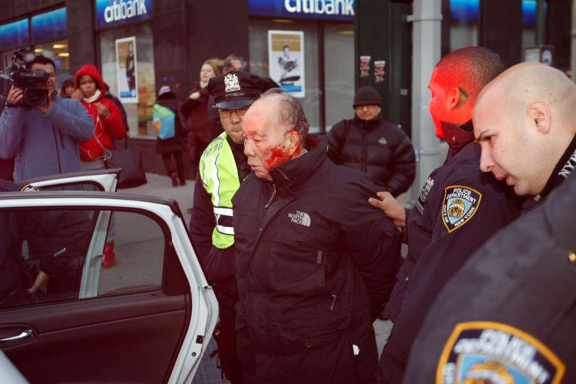 His head bloody, 84 year old Kang Wong is escorted into a police car before being charged with jaywalking. Photo credit: G.N. Miller / NY Post.