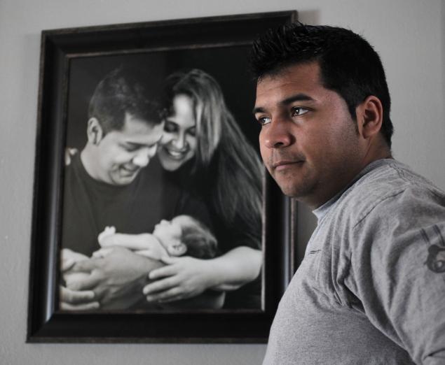 Erick Munoz, husband to Marlise Munoz, stands next to a family portrait. Mr. Munoz is urging Texas lawmakers to honour his wife's wishes and to disconnect her from life support; instead, Texas is forcing Marlise Munoz's body to remain alive to incubate a severely developmentally compromised fetus until 24-26 weeks.