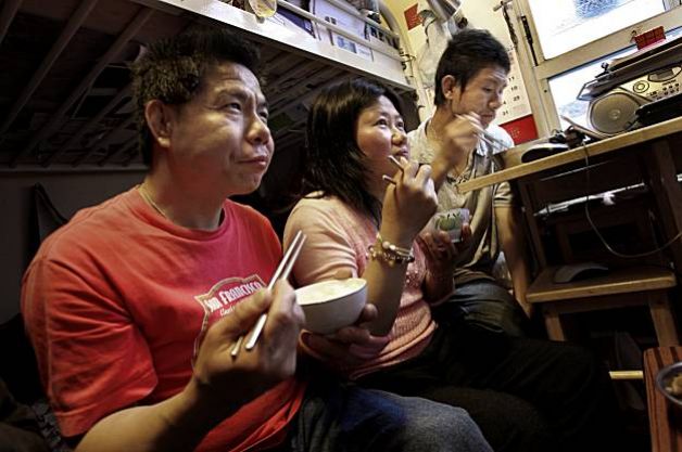 Ba Qi Mo's son and his family eat an evening meal while watching TV in their SRO. The bottom bunk of their bunk bed is used as living space, since there is no room for chairs. (Photo credit: Brant Ward, The Chronicle)