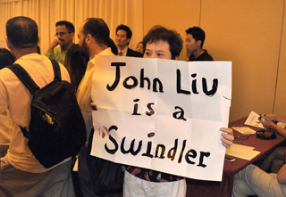 A protester at a recent State Senate candidate's forum holds up a sign expressing his views on State Senate candidate John Liu. Other protesters unfurled a large sign demanding that Liu be arrested "to prevent further harm to the U.S.".