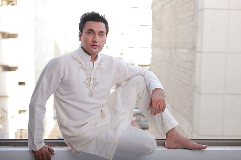 A man models a white shalmar kameez with the intricate embroidery style popular in Pakistan.